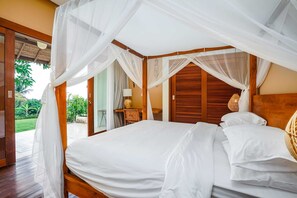 A bedroom with a canopy bed, wooden headboard, and a view of the garden. - Villa Ravenala (Sukasada)