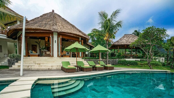 Ein Resort mit Swimmingpool, Liegestühlen und strohgedeckten Gebäuden.