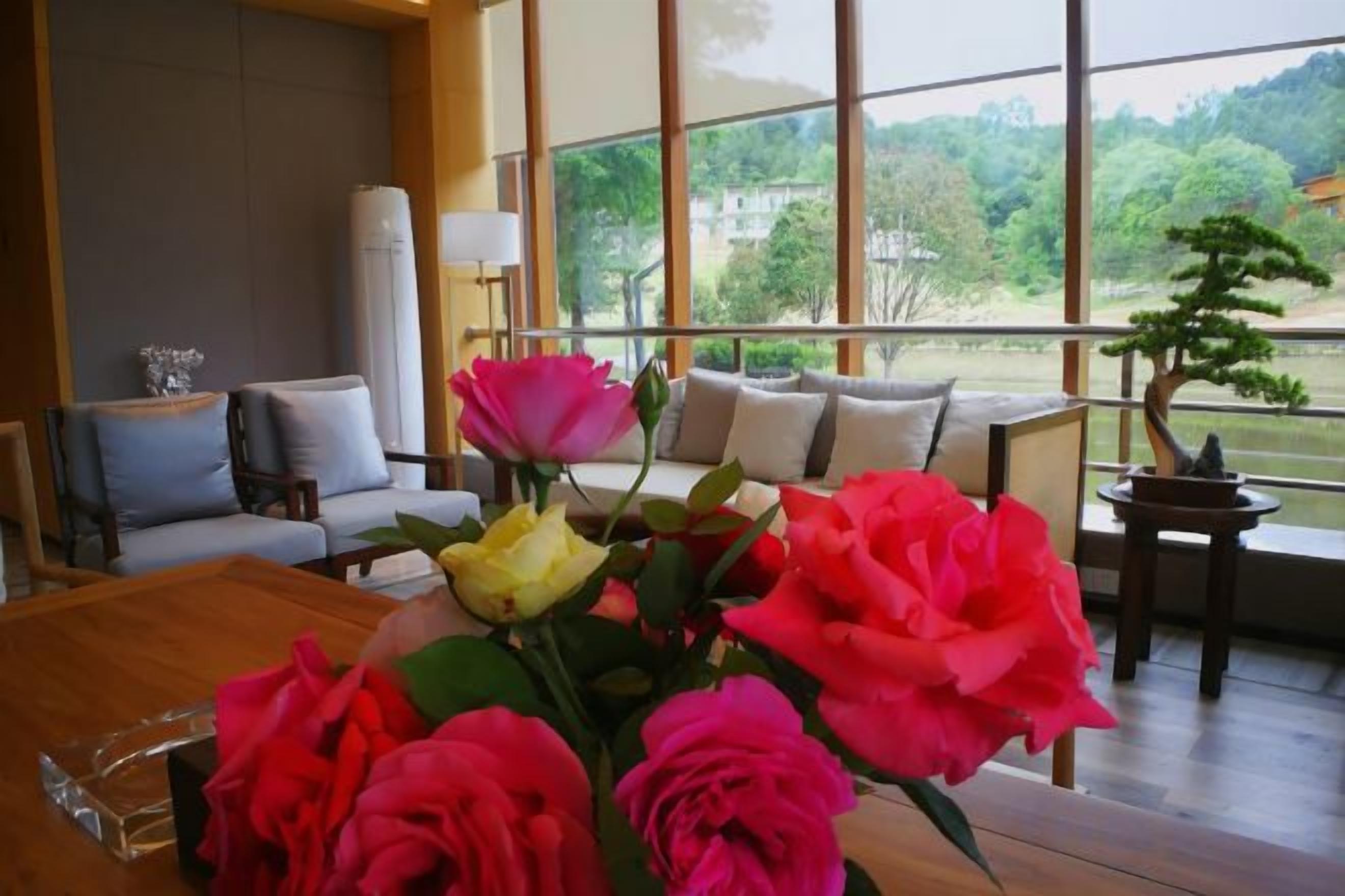 A room with a sofa, a coffee table with flowers, and a view of greenery outside.