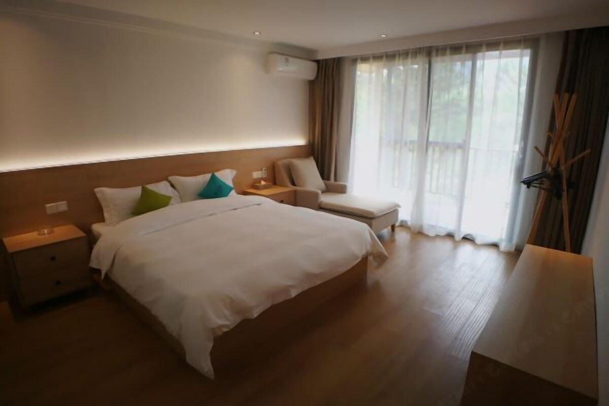 Hotellihuone, jossa on suuri sänky, yöpöytä, tuoli ja ikkuna, jossa on verhot.