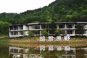 A modern building with a reflection in a body of water, surrounded by greenery.