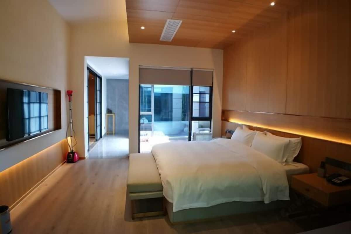 A modern bedroom with a large bed, a TV, and a sliding glass door leading to a balcony.