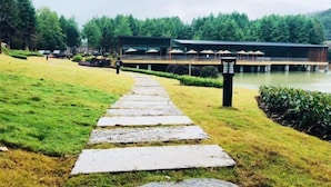 A stone pathway leading to a building with outdoor seating by a lake. - Zhaojun Champaign road Hotel (Xingshan)