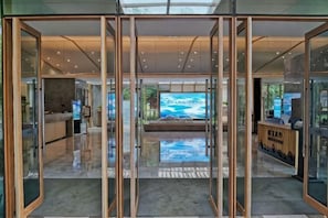 A modern hotel lobby with glass doors, a reception desk, and a large TV screen.