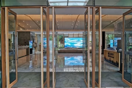 A modern hotel lobby with glass doors, a reception desk, and a large TV screen.. Zhaojun Champaign road Hotel