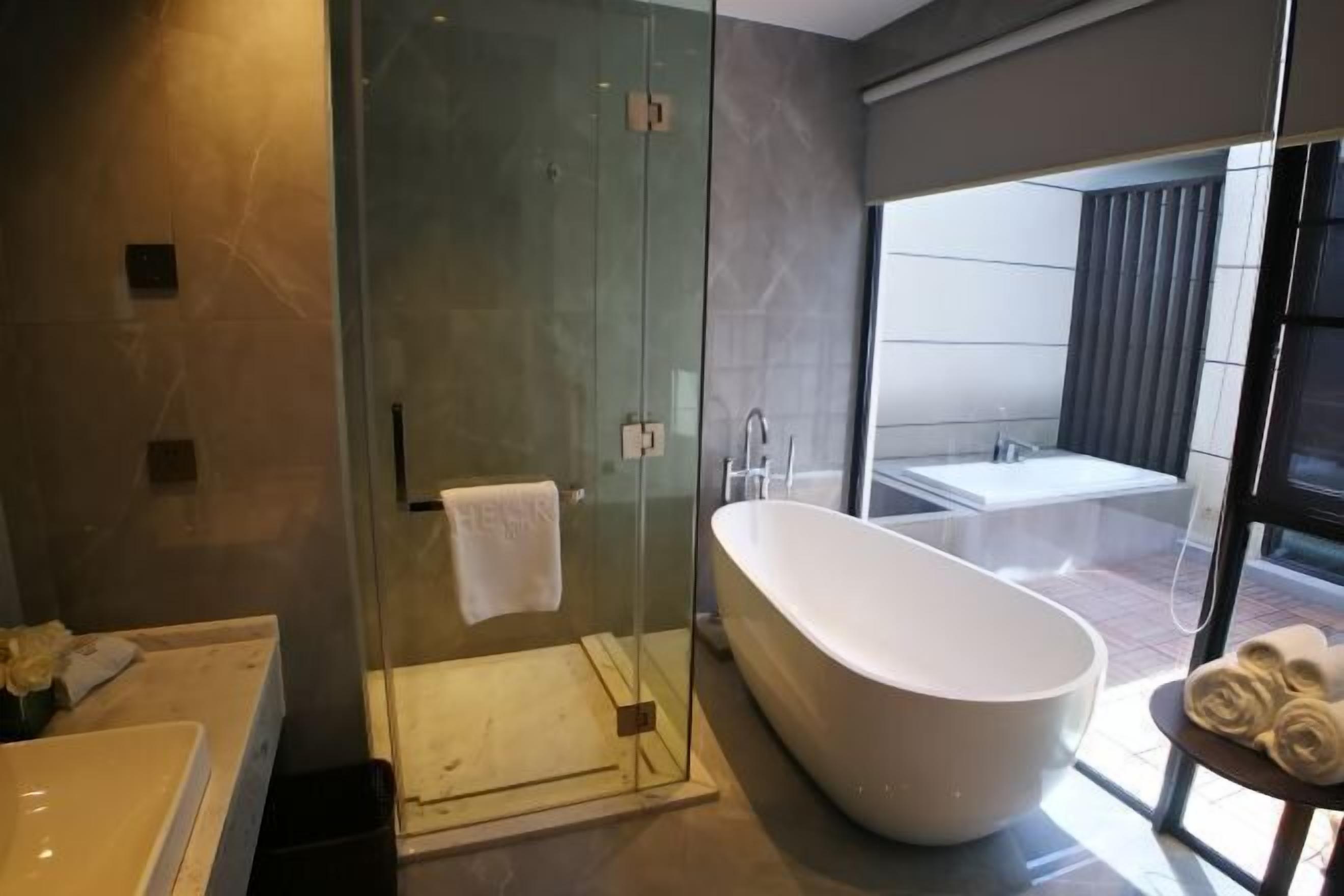 Une salle de bain moderne avec une baignoire sur pieds, une douche à parois de verre et une grande fenêtre offrant une vue sur l’extérieur.
