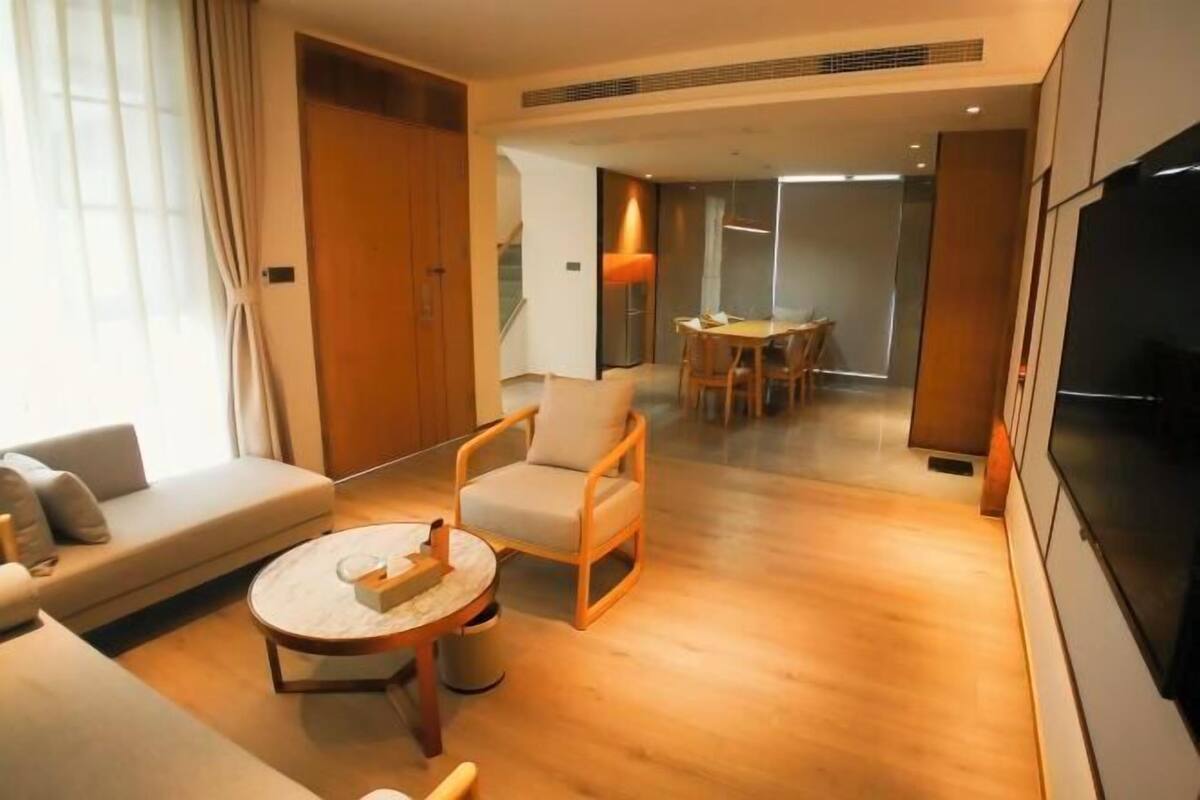 A modern hotel room with a sofa, armchair, round coffee table, and a dining area with a table and chairs.