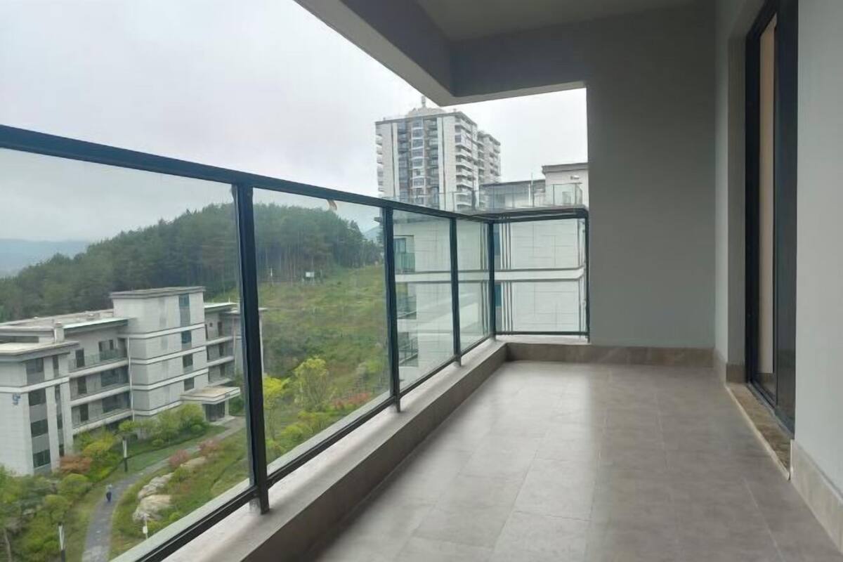 A balcony with a glass railing, a tiled floor, and a view of buildings and greenery.
