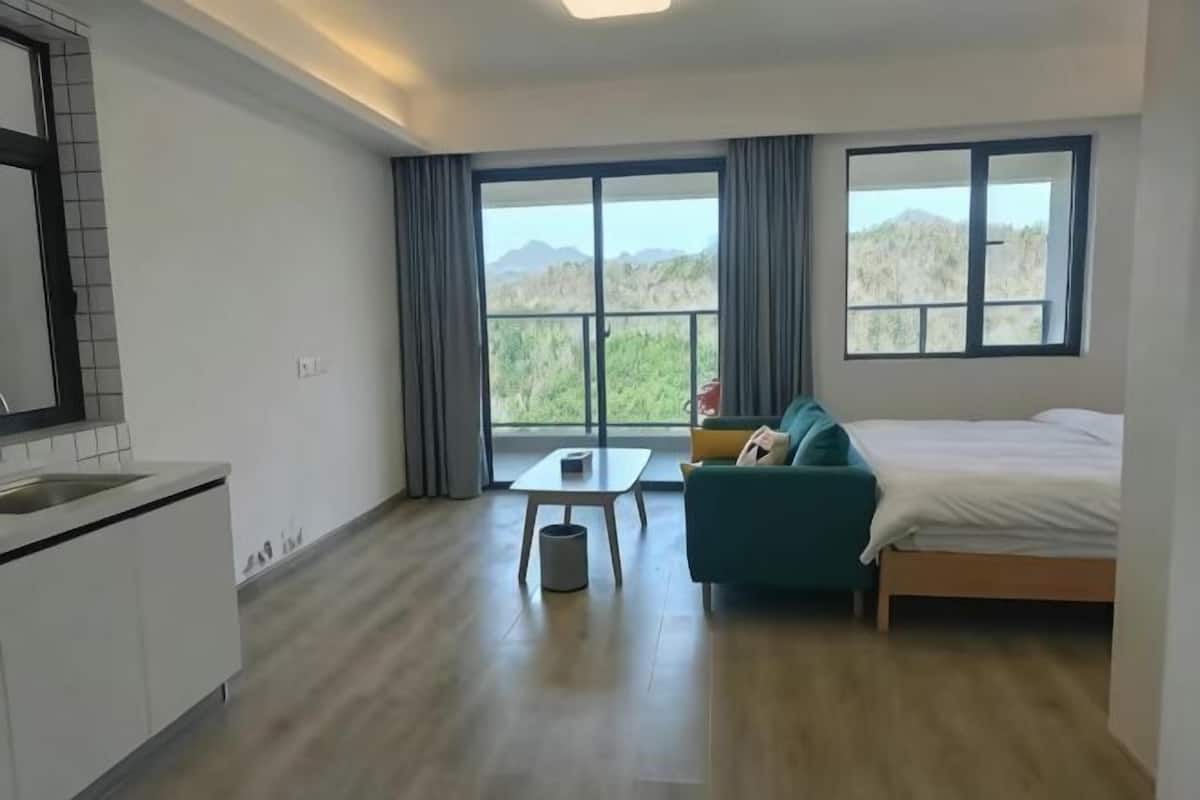 A modern room with a bed, a sofa, a small table, and a kitchen area.