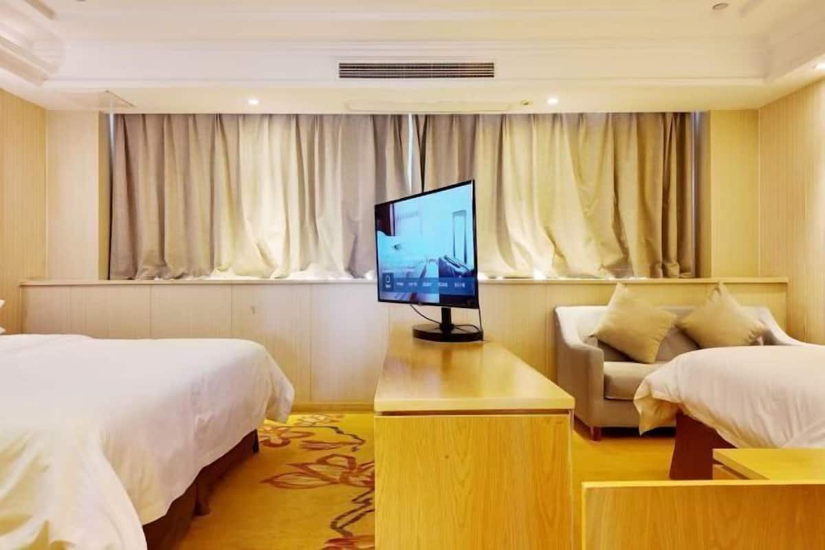 A hotel room with two beds, a TV on a wooden table, and a sofa.