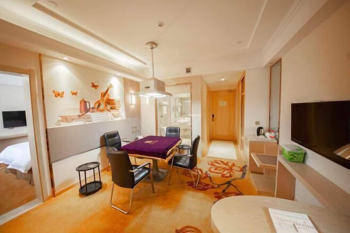 A hotel room with a dining area, a TV, a bed, and a bathroom visible through a glass partition.