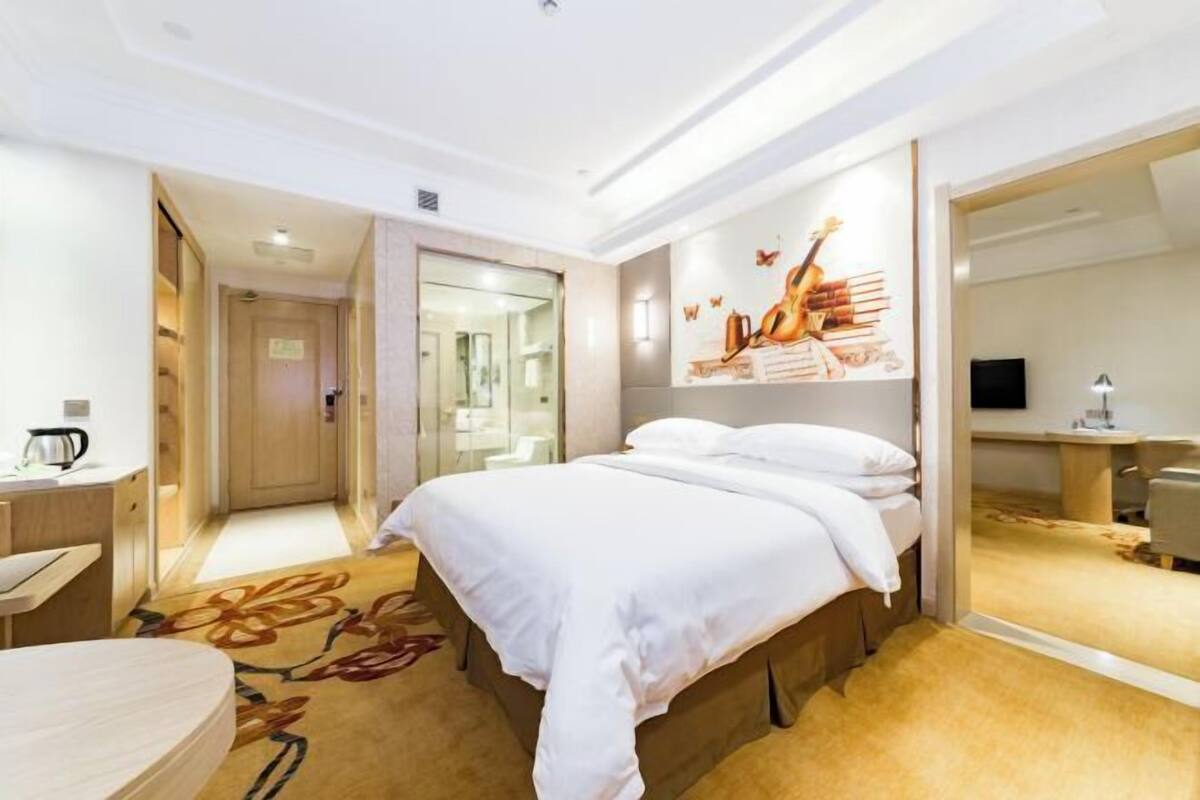 A hotel room with a bed, a desk, a chair, a mirror, and a wall with a guitar artwork.