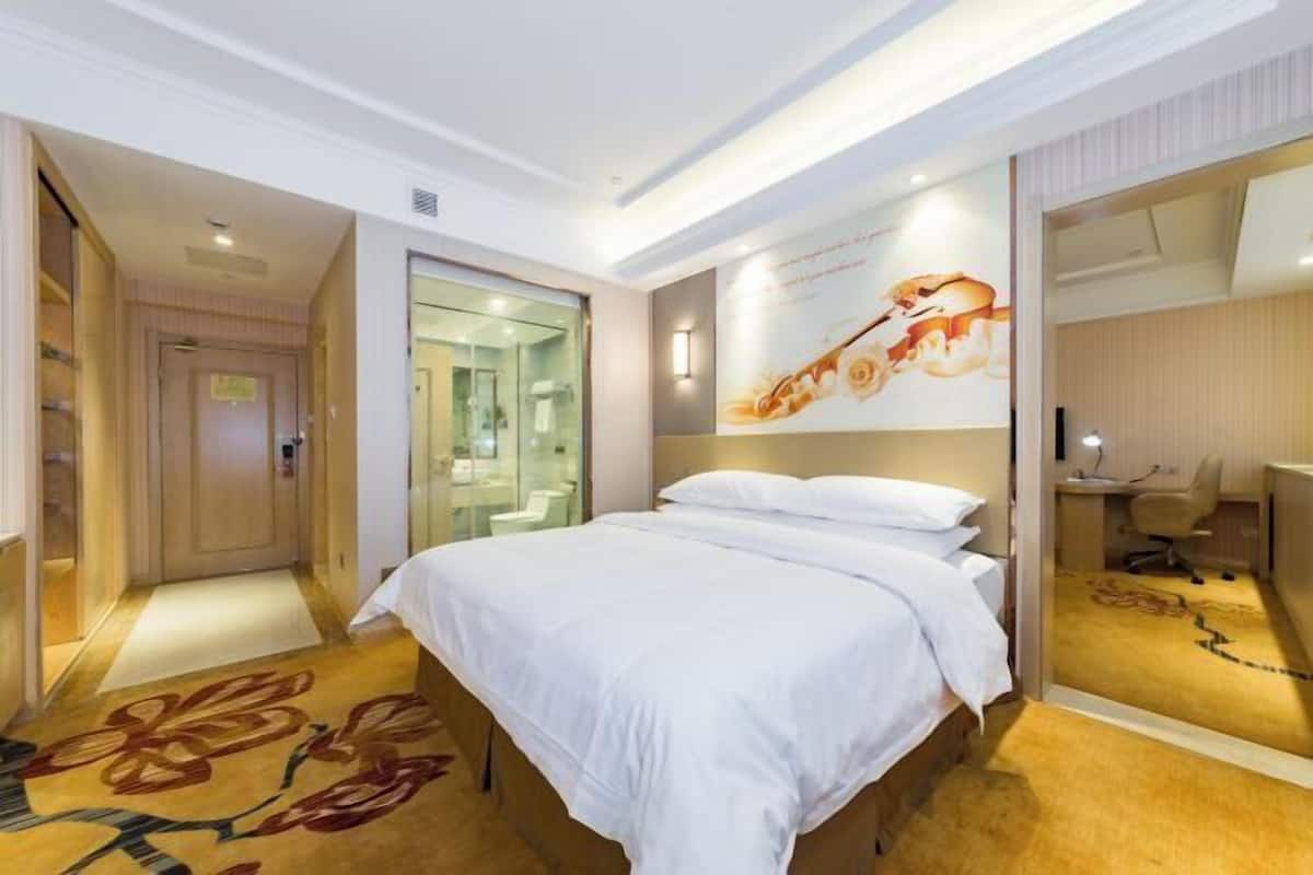 A hotel room with a bed, a desk, a chair, a mirror, and a bathroom with a glass door.