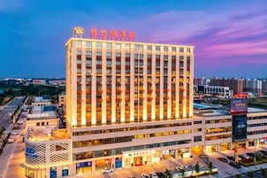 Un hotel de varios pisos con un letrero llamativo en la parte superior, un estacionamiento al frente y una vista despejada del entorno urbano.