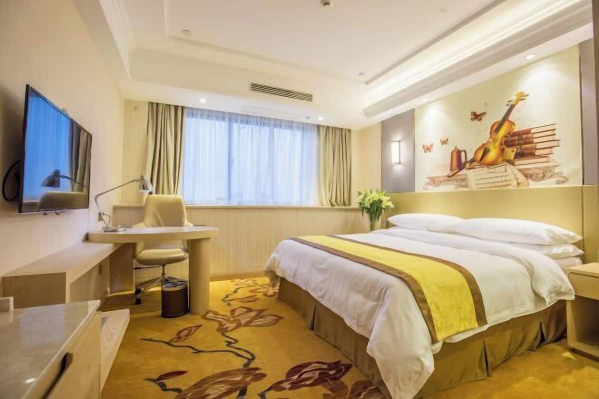 A hotel room with a bed, desk, chair, TV, and a mural on the wall.