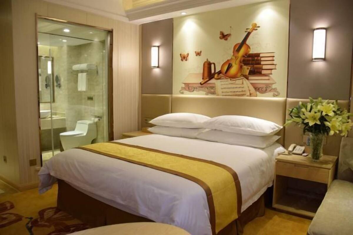 A hotel room with a large bed, a bedside table with a phone, a glass-enclosed shower, and a wall mural.