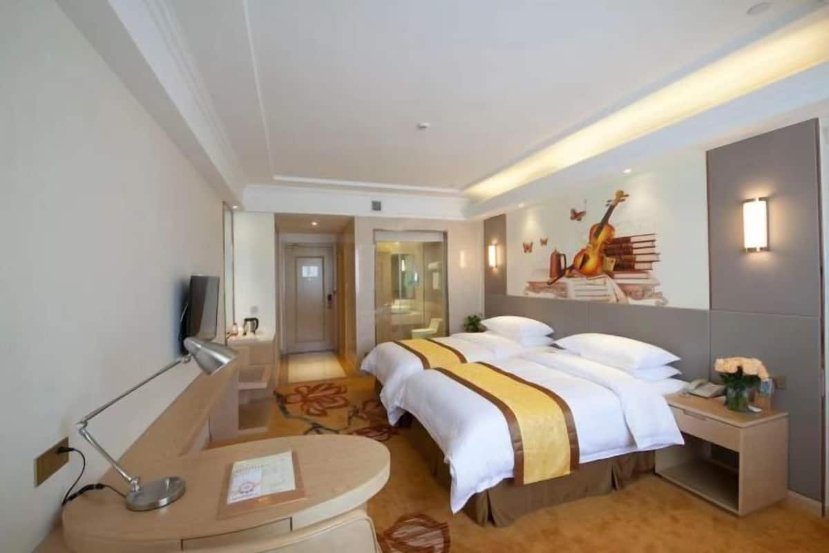 A hotel room with a bed, bedside tables, a desk, a lamp, a TV, and a wall with a guitar and books.