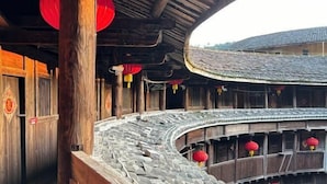 A traditional wooden building with a curved stone roof and red lanterns.