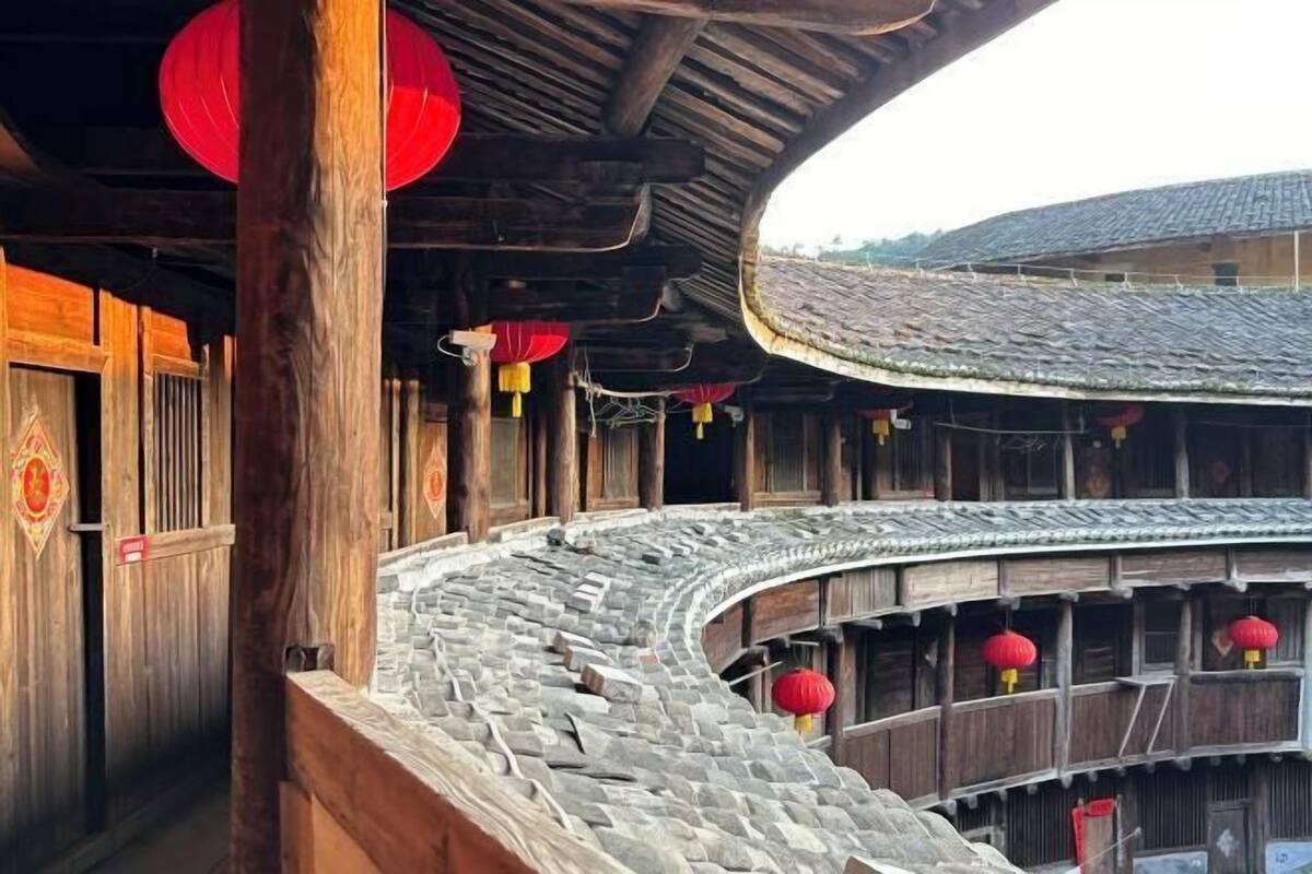 A traditional wooden building with a curved stone roof and red lanterns.