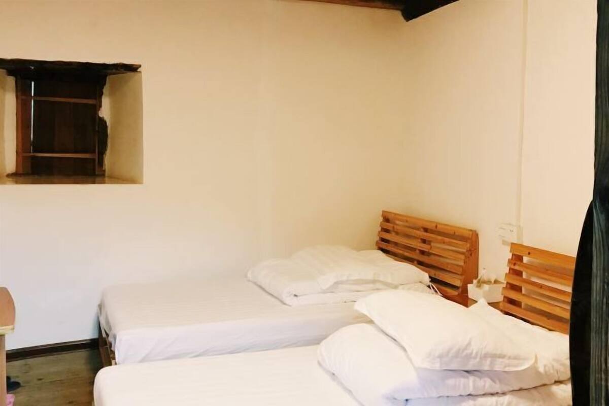 A room with two single beds, wooden headboards, white bedding, a small window, and a wooden door.