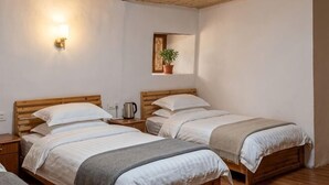 A room with two beds, a wall-mounted light, a small shelf with a plant, and a wooden ceiling. - Yuqinglou Inn (Longyan)