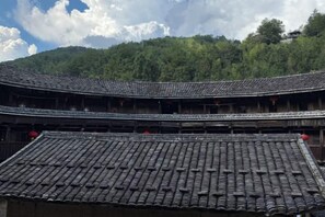 A traditional building with a curved roof and multiple levels, surrounded by lush greenery. - Yuqinglou Inn (Longyan)