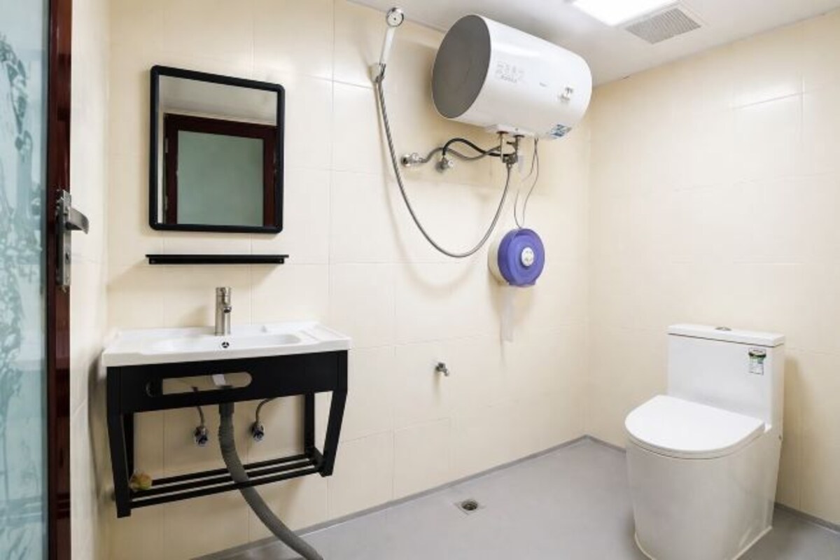 A bathroom with a sink, mirror, toilet, and a hand dryer mounted on the wall.