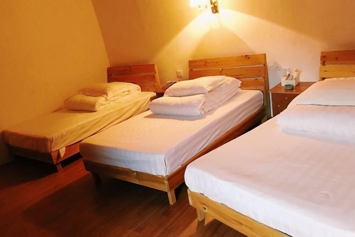 A room with three wooden beds, each with white bedding and pillows, and a nightstand with a lamp.