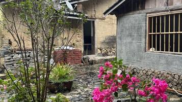 Un edificio tradicional con pared de piedra, una ventana con rejas y una maceta con flores rosas.