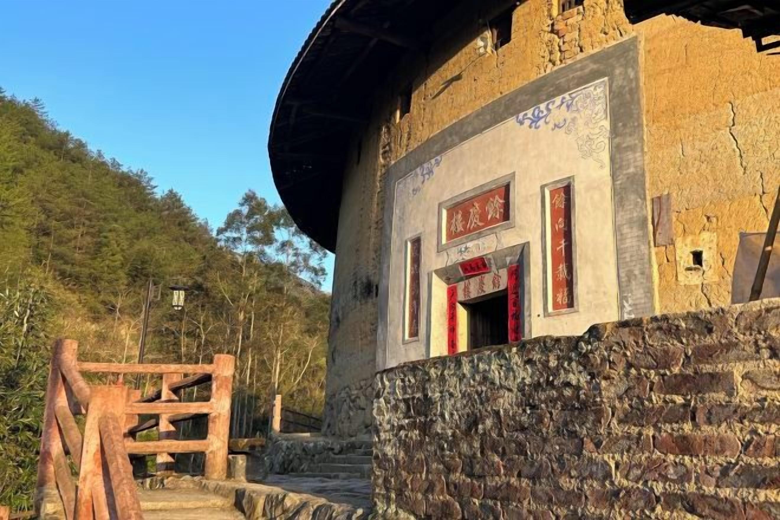 Un edificio tradicional con base de piedra y estructura superior de madera, con una puerta roja y señalización.