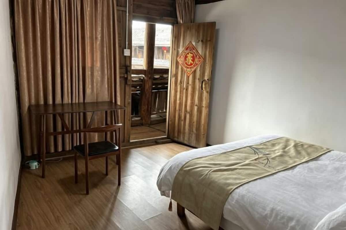 A bedroom with a bed, a wooden desk, a chair, and a wardrobe.