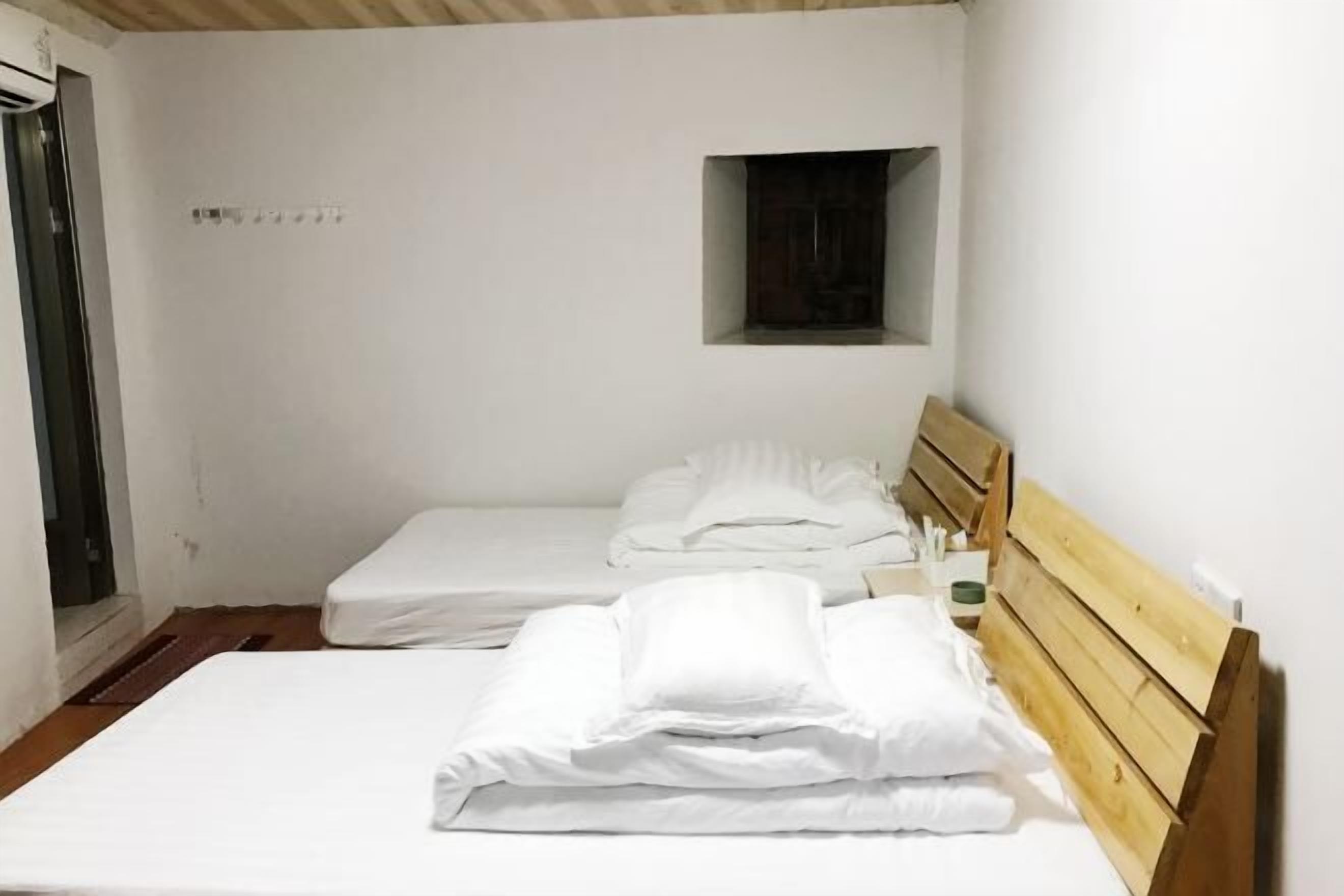 Een kleine, schone kamer met twee eenpersoonsbedden, een houten hoofdbord, een klein raam en een deur.