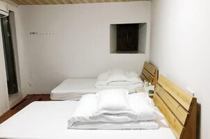 Una habitación pequeña y limpia con dos camas individuales, un cabecero de madera, una ventana pequeña y una puerta.