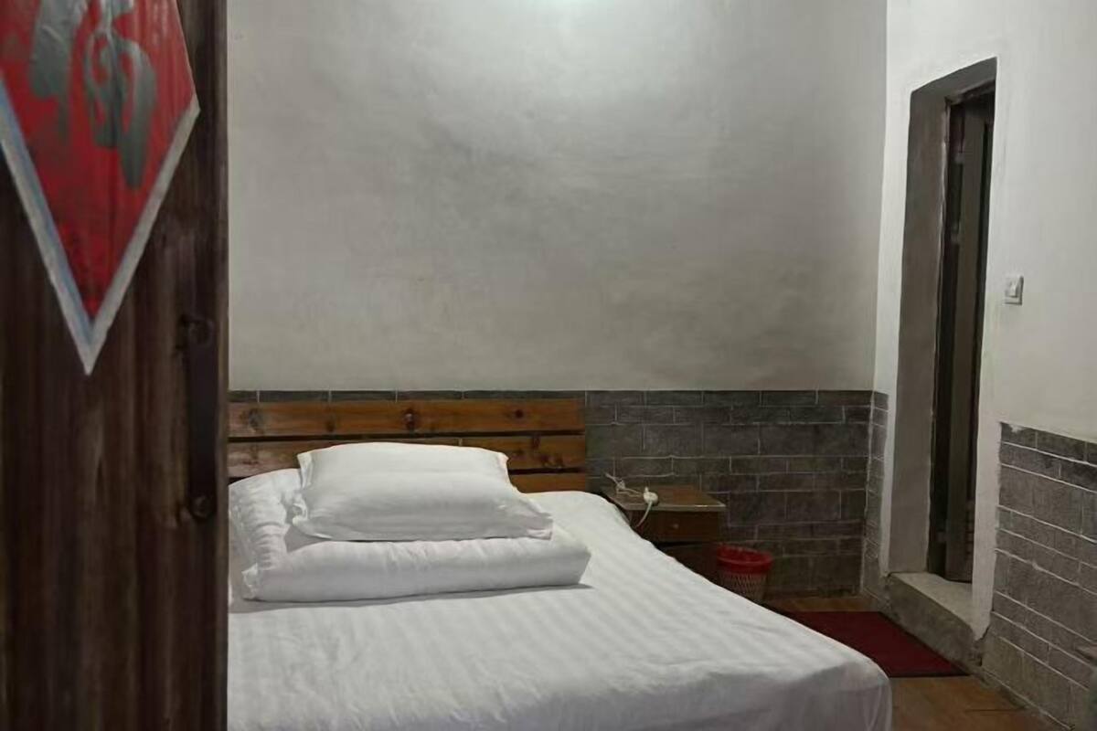 A bedroom with a wooden headboard, a bed with white linens, a nightstand, a red basket, and a door.