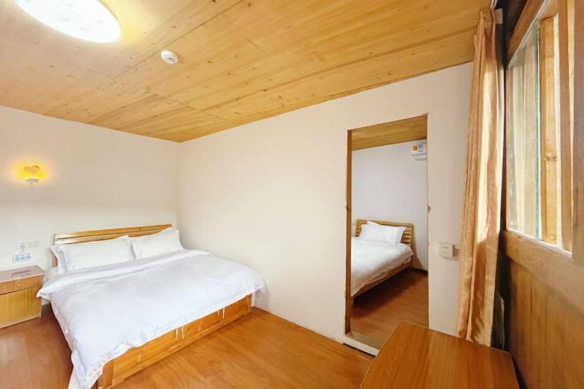 A bedroom with a wooden ceiling, a bed with white bedding, a bedside table, and a mirror.