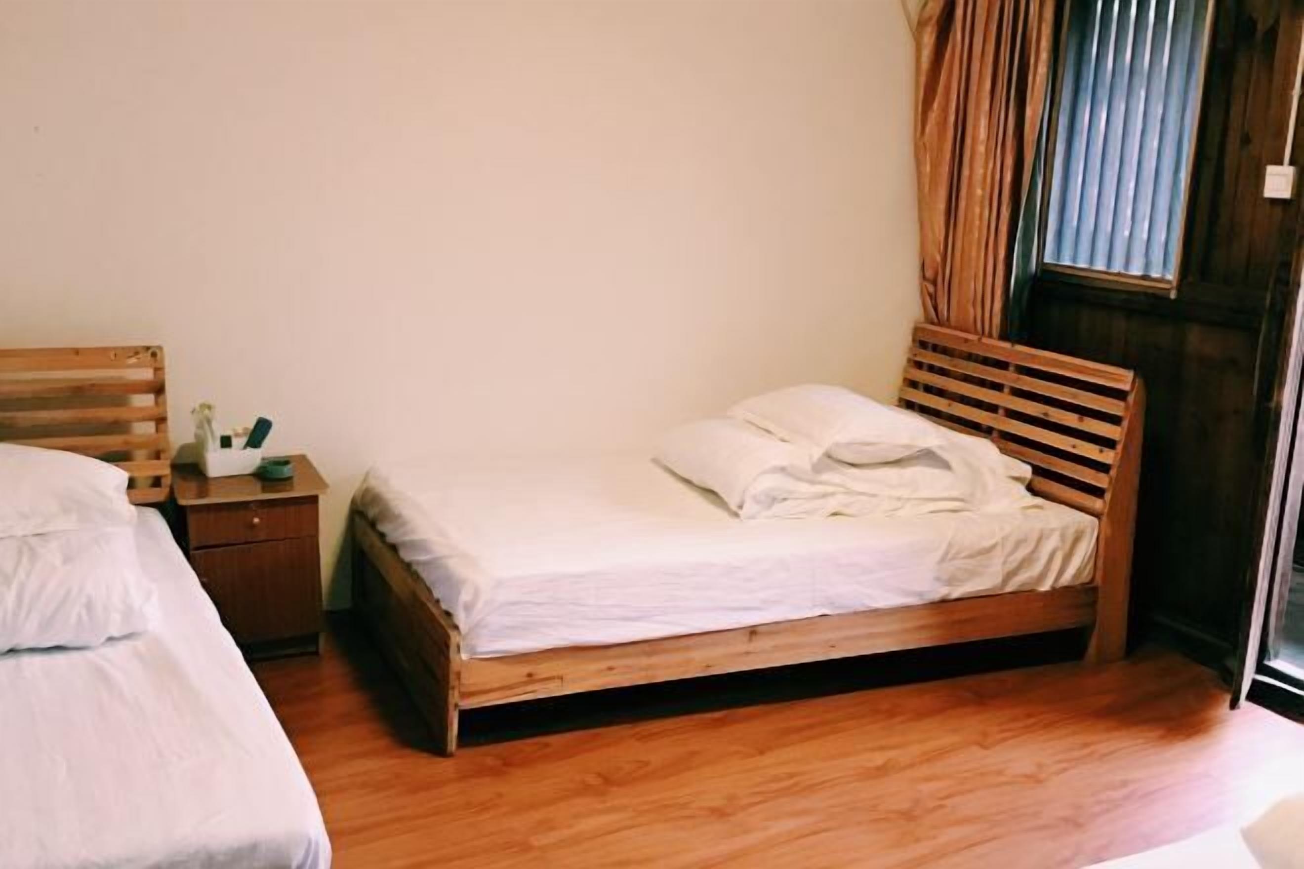 A single wooden bed with white bedding, a wooden nightstand with a lamp, and a window with curtains.