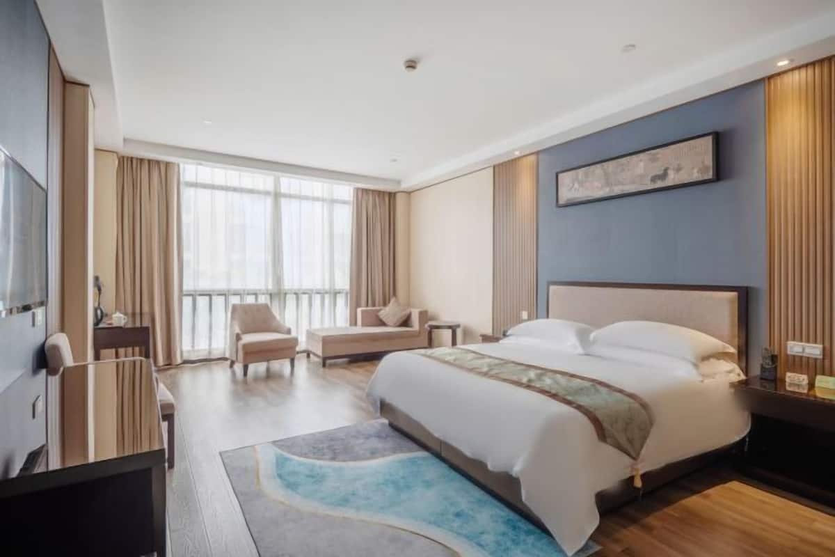 A modern hotel room with a large bed, a sofa, a desk, and a TV.
