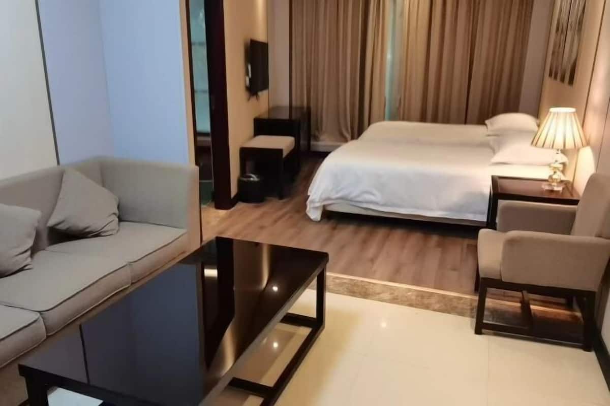 A hotel room with a bed, a sofa, a small table, a lamp, and a TV.