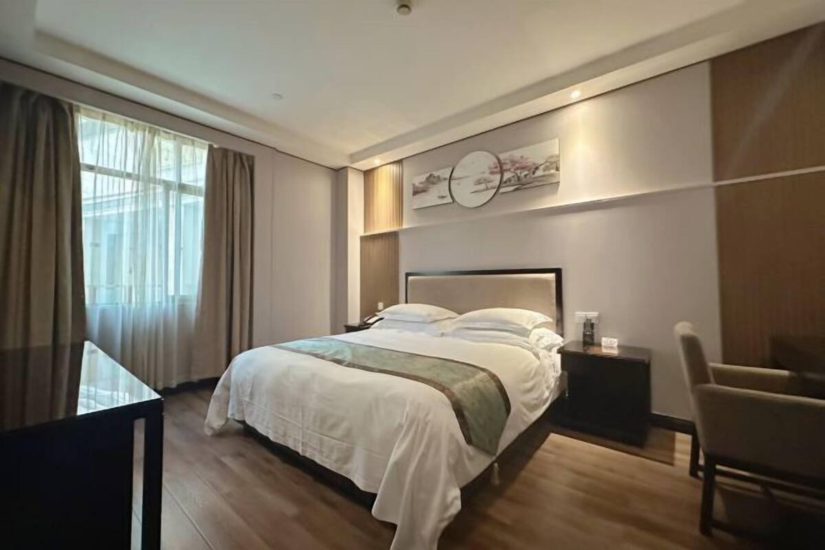 A modern hotel room with a large bed, a bedside table, a chair, and a desk.