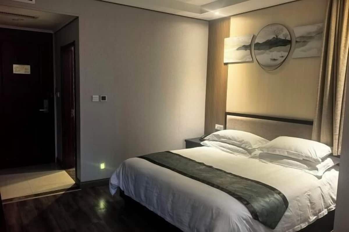 A hotel room with a bed, bedside tables, a wall-mounted artwork, and a door.