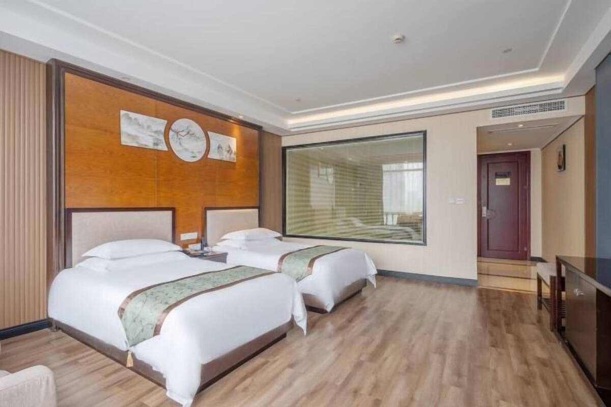 A hotel room with two beds, a large window, and a wooden floor.