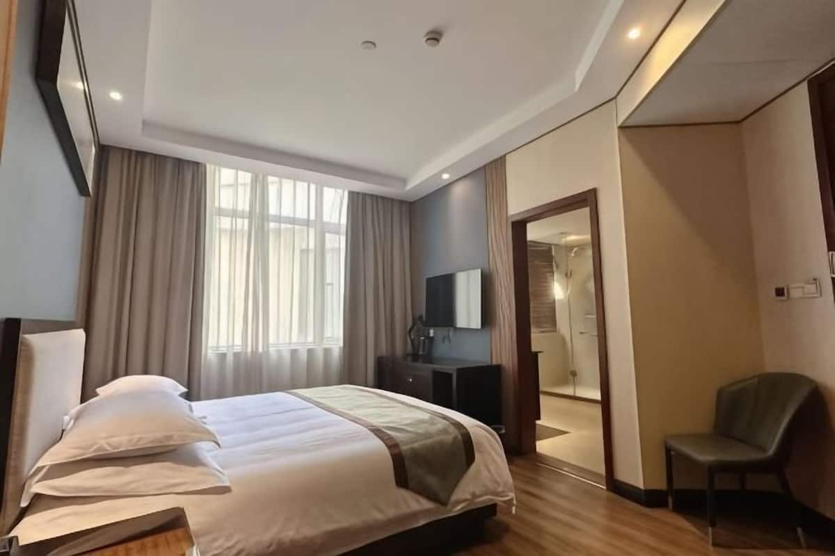 A hotel room with a bed, a chair, a desk, a mirror, and a window.