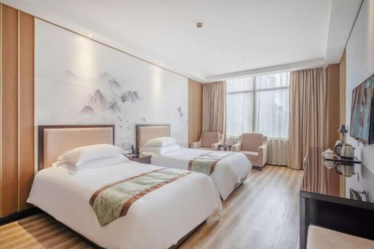 A hotel room with two beds, a desk, a chair, and a large window with curtains.