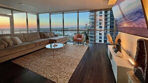 Una sala de estar moderna con un sofá grande, una mesa de centro y vistas a un paisaje urbano a través de amplios ventanales.