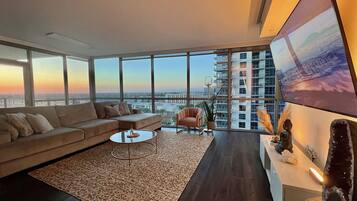 Uma sala de estar moderna com um sofá grande, uma mesa de centro e vista para o horizonte urbano através de amplas janelas.