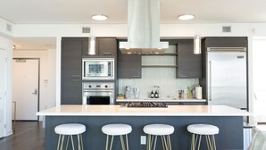 Una cocina moderna con una isla central, taburetes de bar, electrodomésticos de acero inoxidable y un amplio ventanal.