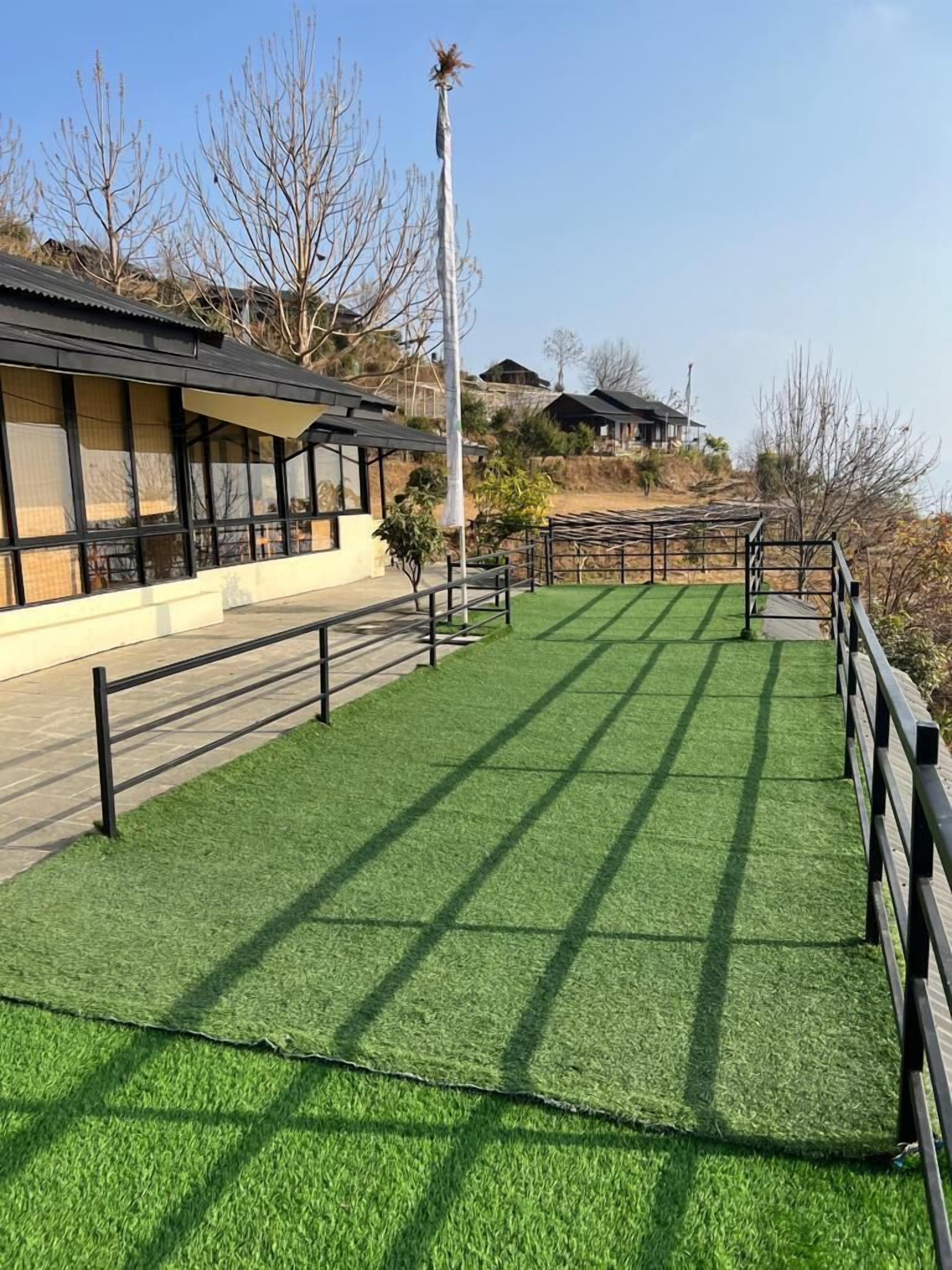 A building with a flat roof, a fenced outdoor area with artificial grass, and a clear sky.