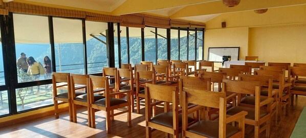 A conference room with wooden chairs and tables, large windows with a mountain view, and a whiteboard on the wall.