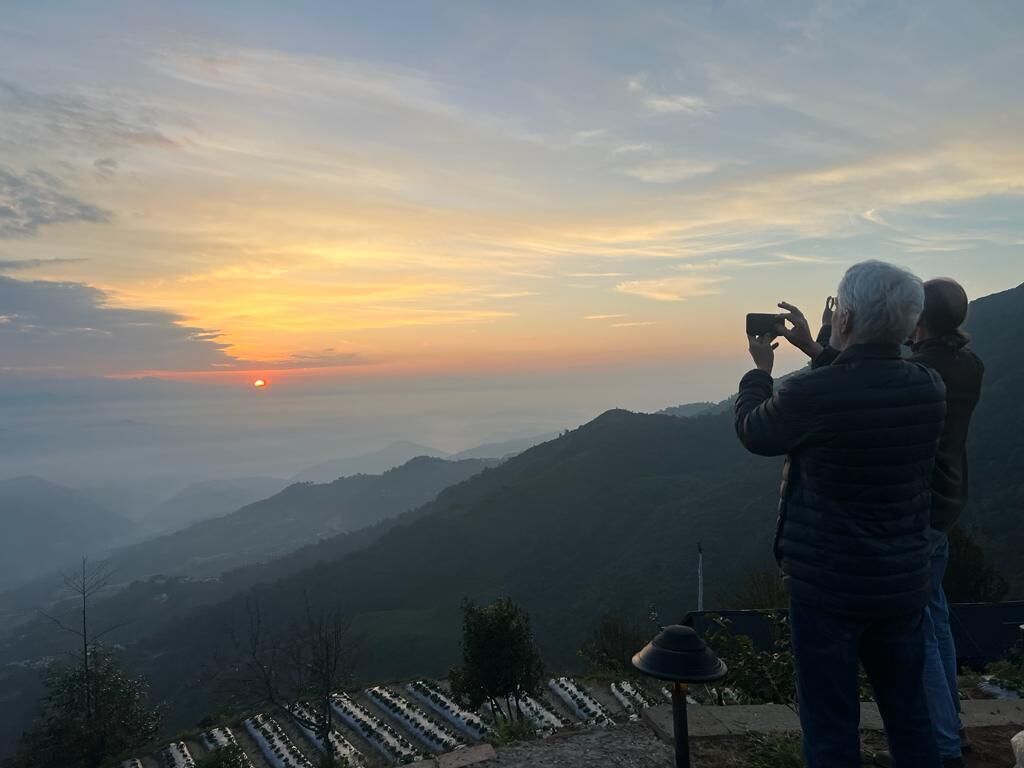 A person taking a photo of a sunset over a mountainous landscape.