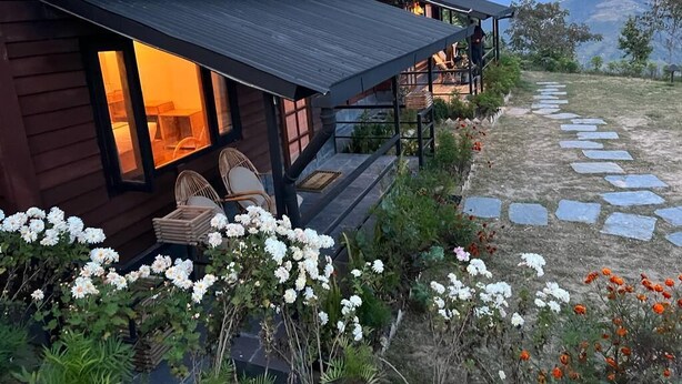 Una cabaña de madera con un porche, un camino de piedra y plantas en flor.